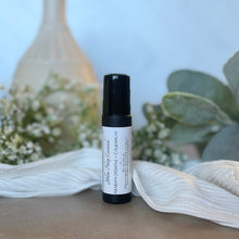 Load image into Gallery viewer, A small black cylindrical bottle with a white label reading 'Yellow Harp Essentials Rollerball Perfume Oil Arabian Jasmine + Galbanum' stands on a tabletop surrounded by soft white fabric, small white flowers, green leaves, and a blurred decorative vase in the background.