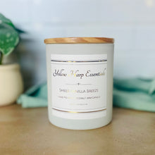 Load image into Gallery viewer, White glass jar with wood lid and Yellow Harp Essentials label with Sheer Vanilla Breeze scent and greenery background