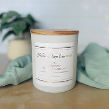 Load image into Gallery viewer, White glass jar with wood lid with Yellow Harp Essentials label and Gardenia + Orange Blossom scent with greenery in background
