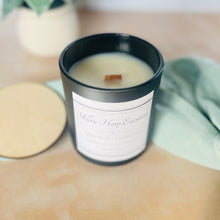 Load image into Gallery viewer, Black glass candle jar with wood lid and white background with plant and cloth