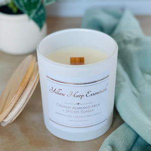 highly scented creamy almond milk and spiced tonka coconut wax candle with crackling wood wick in reusable white glass jar and wood lid