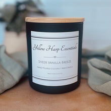 Load image into Gallery viewer, Candle with a label reading 'Yellow Harp Essentials Sheer Vanilla Breeze' on a wooden surface.