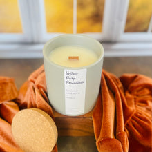 Load image into Gallery viewer, Gray glass candle jar with cork lid and white label that says “yellow harp essentials smoked lavender and amber coconut wax candle” on wood table and fall leaves out a window 
