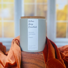 Load image into Gallery viewer, Gray glass candle jar with cork lid and white label that says “yellow harp essentials smoked lavender and amber coconut wax candle“ on wood table with fall colored trees out a back window
