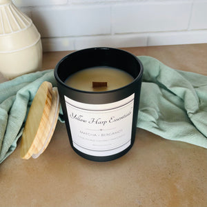 yellow harp essentials highly scented hand poured coconut wax candle with crackling wood wick in glass black jar with wood lid. Matcha and bergamot scent