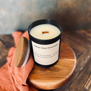 Candle with wooden lid held by a hand on a wooden surface, featuring 'Yellow Harp Essentials' branding.