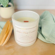 Load image into Gallery viewer, White glass jar with wood lid with Yellow Harp Essentials label and Gardenia + Orange Blossom scent with greenery in background
