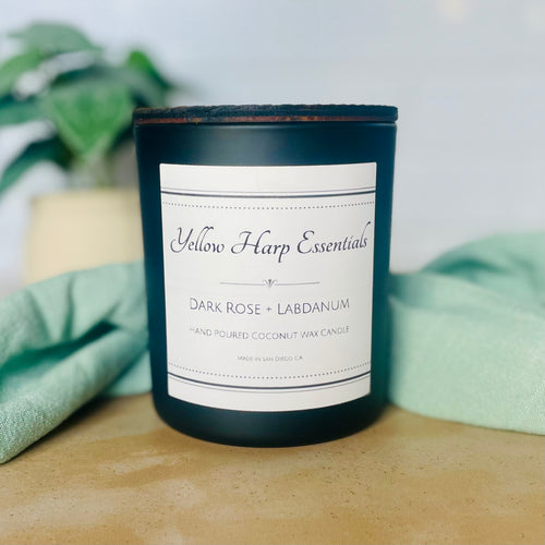 Black glass candle jar with wood lid and white background with plant and cloth