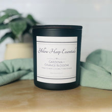 Load image into Gallery viewer, black glass jar with Yellow Harp Essentials on label and gardenia + orange blossom scent with greenery in background
