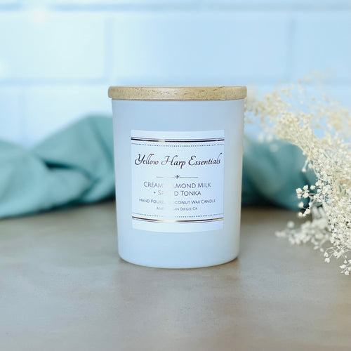 highly scented creamy almond milk spiced tonka coconut wax candle with crackling wood wick in reusable white glass jar and wood lid