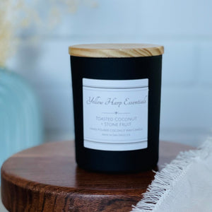 highly scented toasted coconut and stone fruit coconut wax candle with crackling wood wick in reusable black glass jar and wood lid