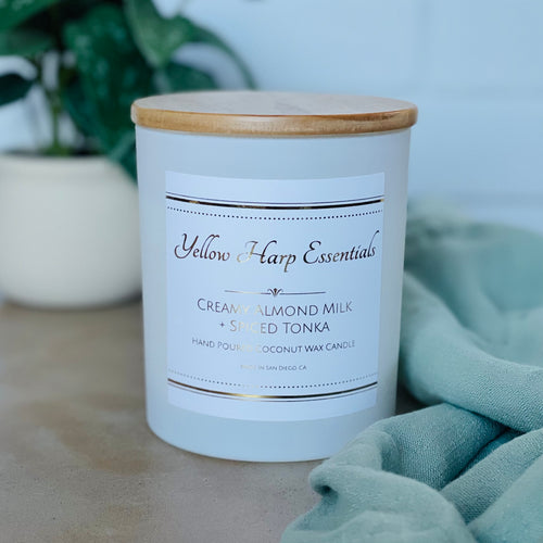 highly scented creamy almond milk and spiced tonka coconut wax candle with crackling wood wick in reusable white glass jar and wood lid