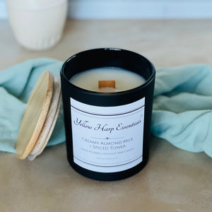 highly scented creamy almond milk and spiced tonka coconut wax candle with crackling wood wick in reusable black glass jar and wood lid