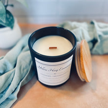 Load image into Gallery viewer, Candle with wooden wick in a black container on a wooden surface with a blurred background

