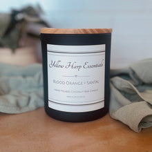 Load image into Gallery viewer, Black candle with a wooden lid on a surface, featuring 'Yellow Harp Essentials' branding.
